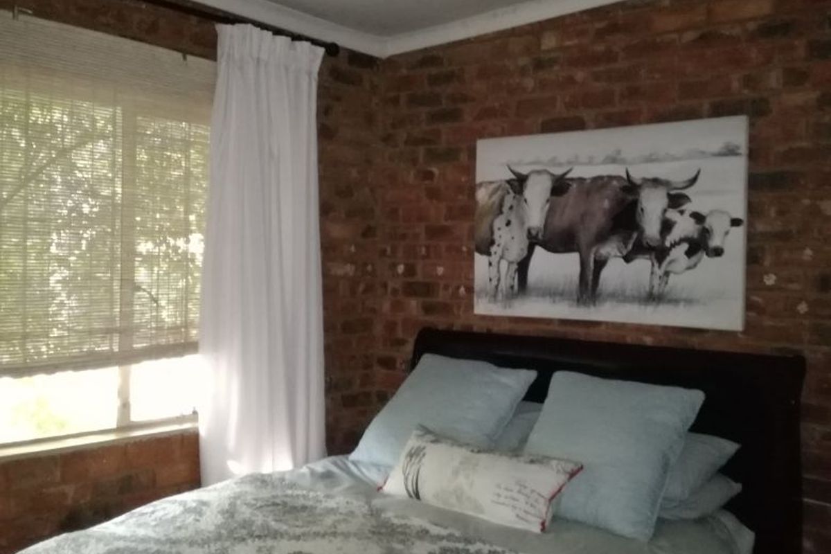 A bedroom featuring an exposed brick feature wall, a ceiling fan, and natural light through window blinds.