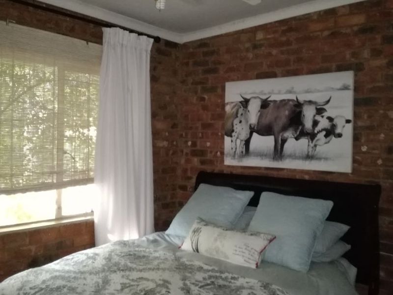 A bedroom featuring an exposed brick feature wall, a ceiling fan, and natural light through window blinds.