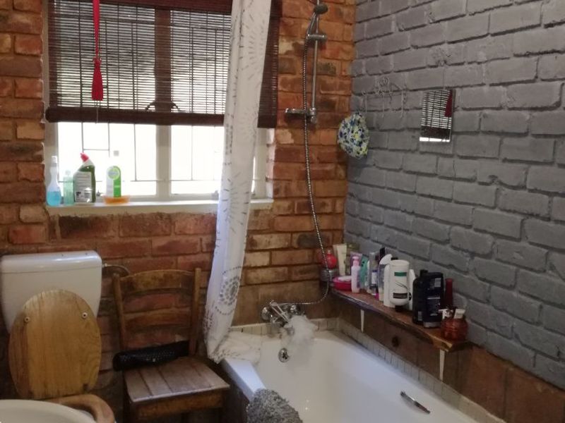 Bathroom featuring a mix of exposed and painted brick walls, a standard bathtub with shower attachment, toilet, and washbasin.