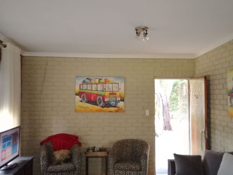 A living room featuring exposed brick walls, a timber ceiling beam, and tiled flooring, with direct access to an outdoor area.
