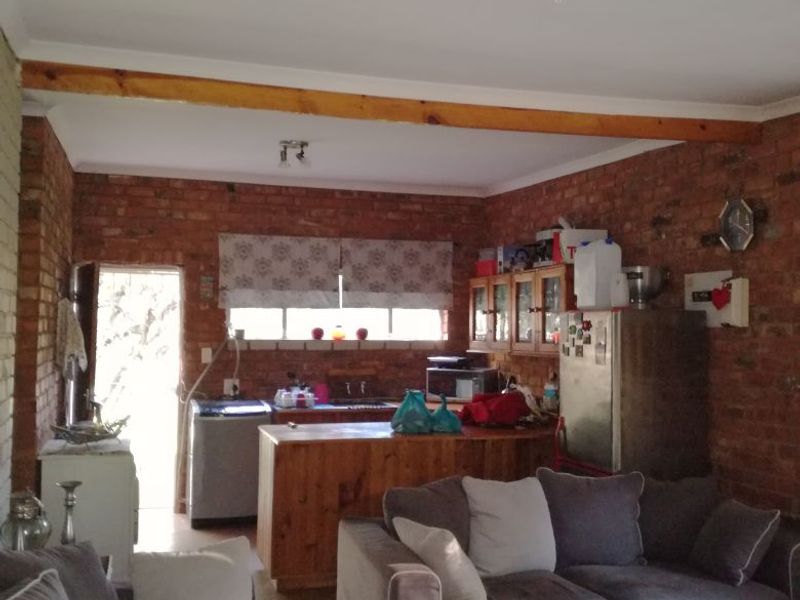 Open plan living and kitchen area featuring exposed brick walls, timber ceiling beams, and tiled flooring in a functional layout.