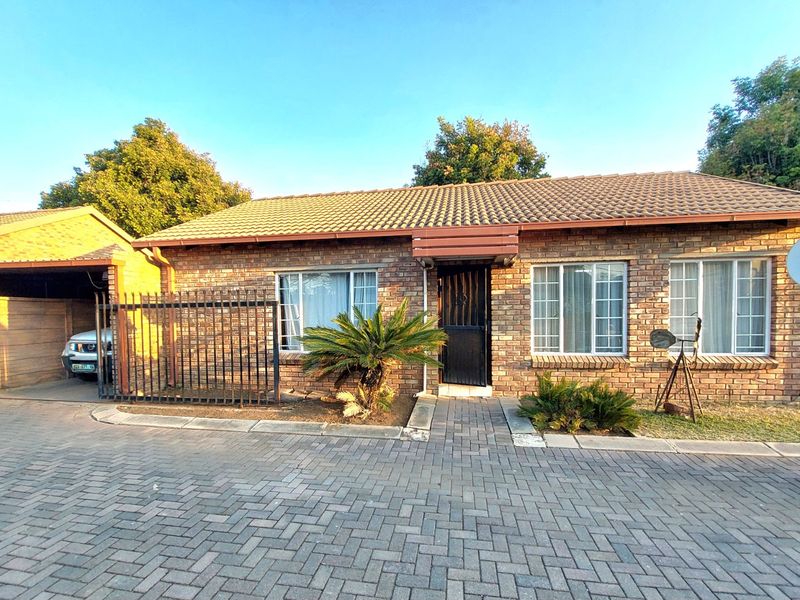 Front elevation of a face brick townhouse featuring a paved driveway, attached carport, and secure entrance.