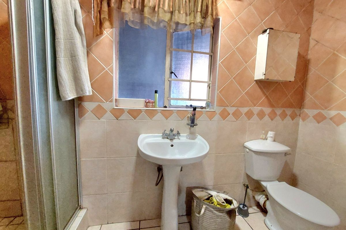 A dated bathroom featuring a pedestal basin, toilet, and shower enclosure with traditional tiled finishes.