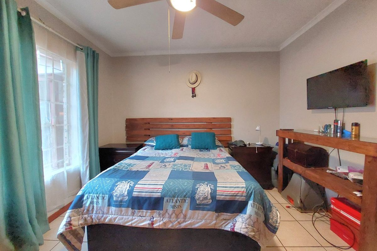A functional bedroom featuring tiled flooring, a ceiling fan, and a built-in wooden headboard, offering a comfortable and practical living space.