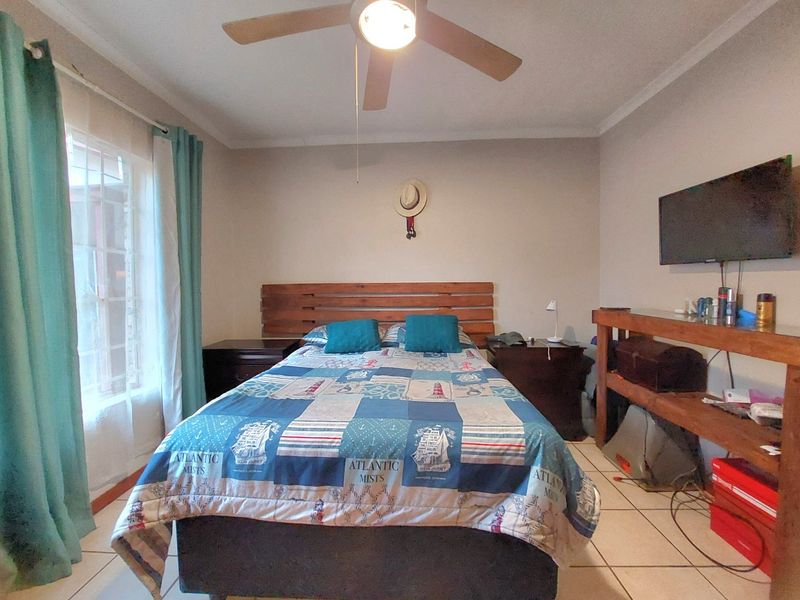 A functional bedroom featuring tiled flooring, a ceiling fan, and a built-in wooden headboard, offering a comfortable and practical living space.