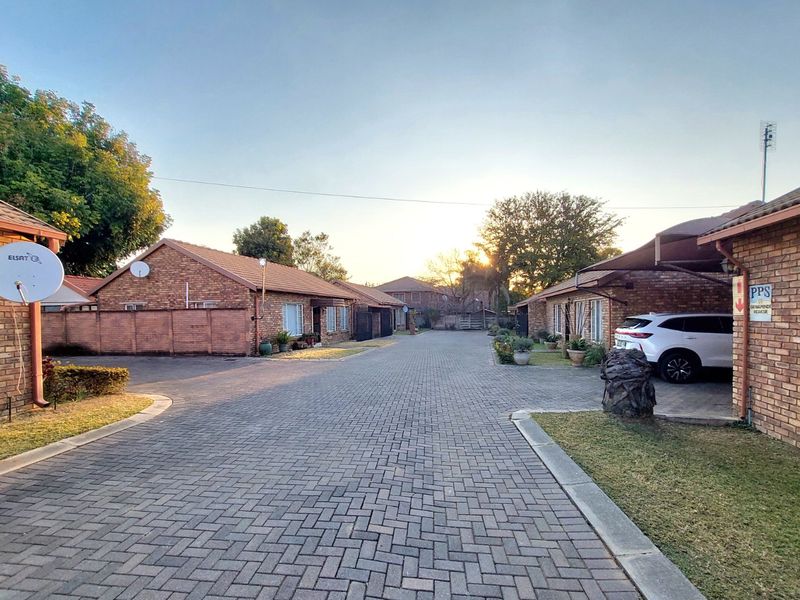 A view of the complex driveway featuring face brick townhouse facades, paved surfaces, and covered parking areas.