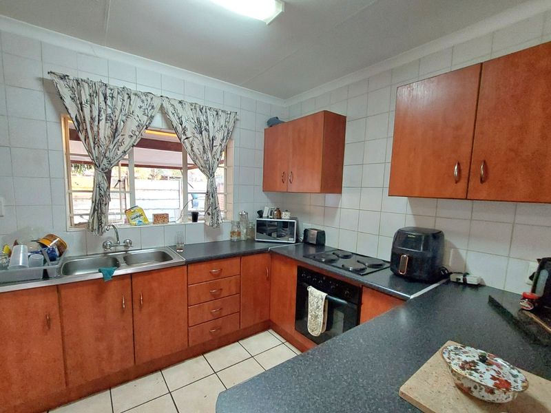 A functional kitchen featuring wooden cabinetry, a double basin sink, built-in oven, and electric hob with tiled splashbacks and flooring.