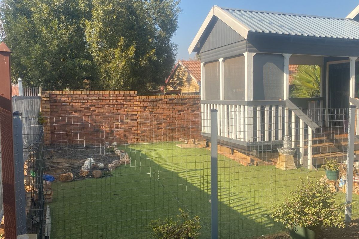 A rear garden area featuring an artificial lawn, brick boundary wall, and a raised timber gazebo structure with a corrugated metal roof.