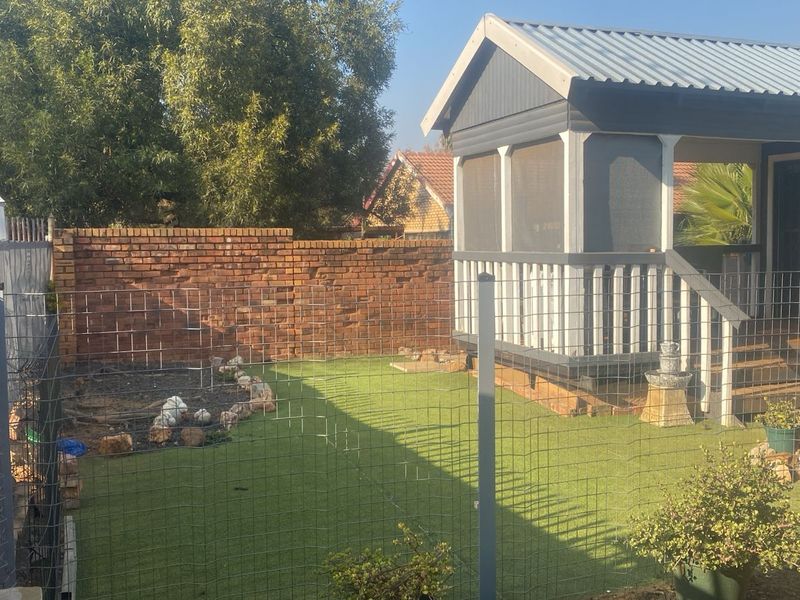 A rear garden area featuring an artificial lawn, brick boundary wall, and a raised timber gazebo structure with a corrugated metal roof.