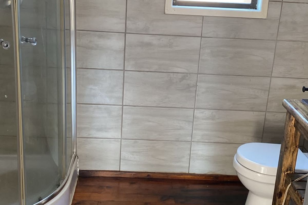 A bathroom featuring a corner shower enclosure, toilet, and tiled wall finishes with dark timber flooring.