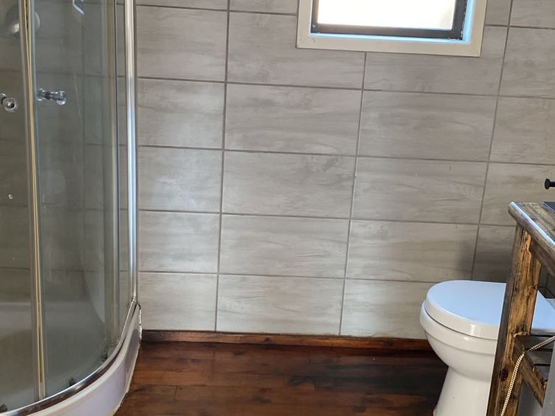 A bathroom featuring a corner shower enclosure, toilet, and tiled wall finishes with dark timber flooring.