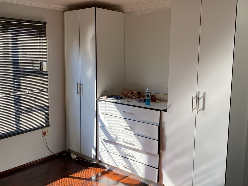 A bedroom featuring built-in white cupboards with integrated drawers, hardwood flooring, and venetian blinds.