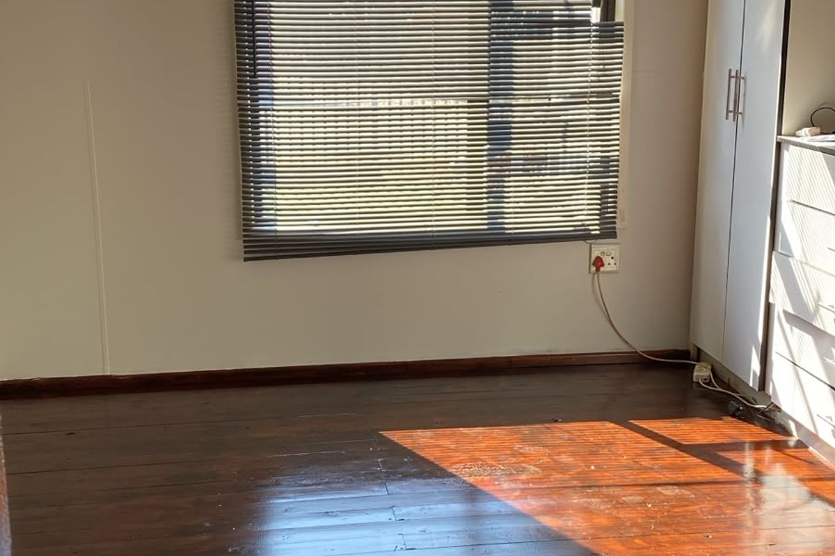 A bright, empty bedroom featuring polished timber flooring, built-in wardrobe storage, and venetian blinds, offering a clean canvas for personalization.
