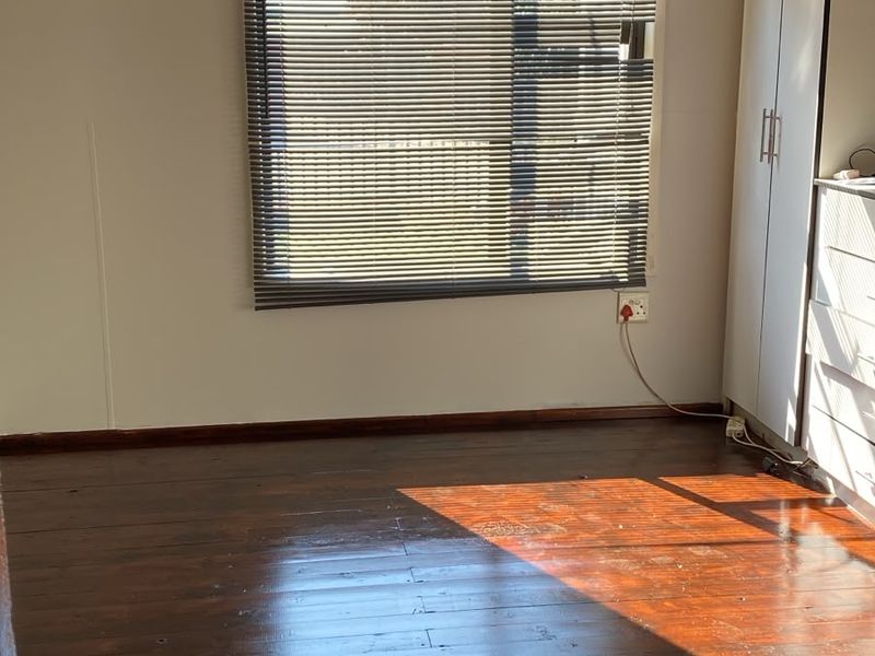 A bright, empty bedroom featuring polished timber flooring, built-in wardrobe storage, and venetian blinds, offering a clean canvas for personalization.