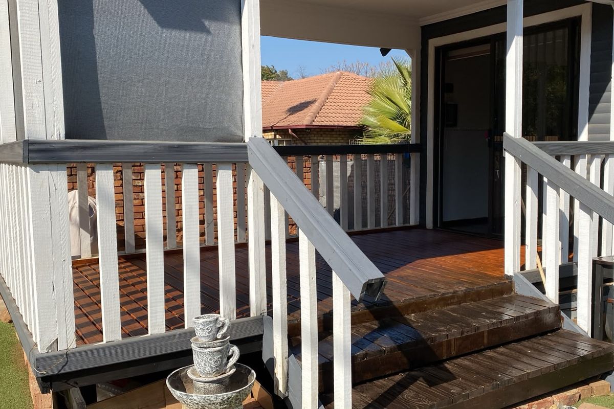 A raised timber deck patio featuring a painted balustrade and direct access to the interior via a sliding glass door.