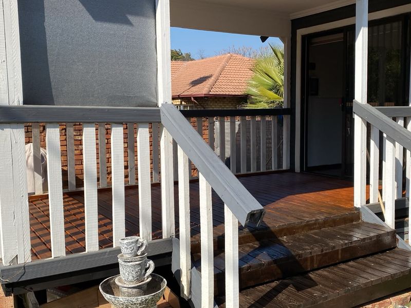 A raised timber deck patio featuring a painted balustrade and direct access to the interior via a sliding glass door.