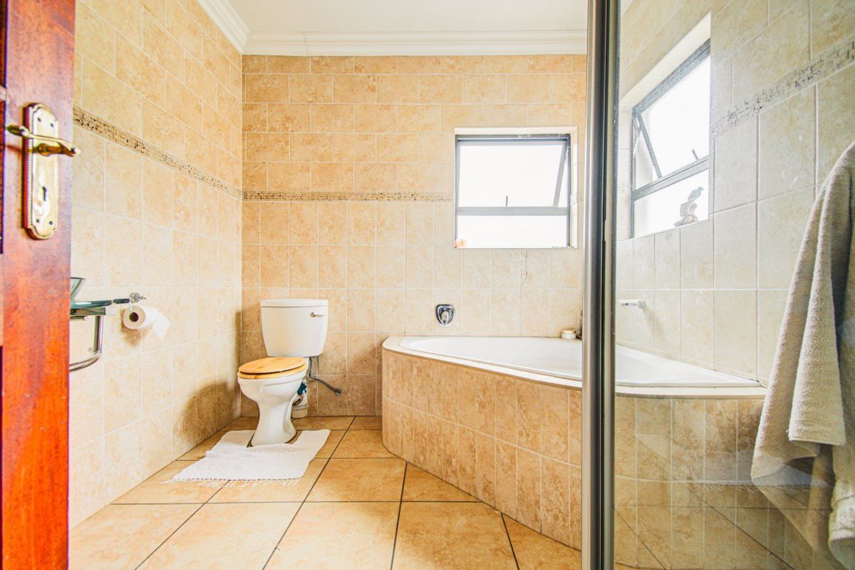 A functional bathroom featuring a corner bathtub, tiled walls and flooring, and a separate shower enclosure with natural light from a top-hung window.