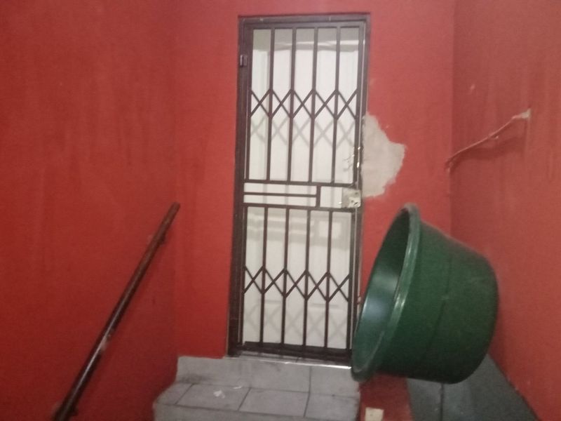 An interior entrance area featuring a security gate, tiled steps, and a handrail, currently showing signs of wall damage and exposed wiring.