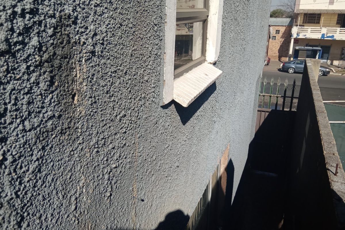 Exterior view of the building side showing textured plaster wall, metal window frame, and concrete sill with visible signs of wear and cracking.