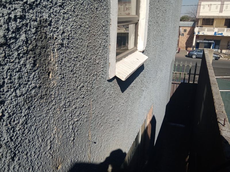 Exterior view of the building side showing textured plaster wall, metal window frame, and concrete sill with visible signs of wear and cracking.