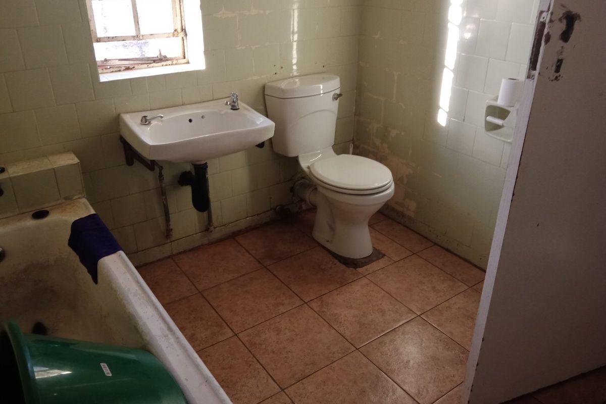A dated bathroom featuring a bathtub, wall-mounted basin, and toilet, requiring renovation and cosmetic updates to improve its overall condition and appeal.
