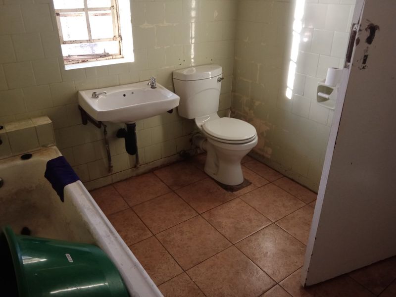 A dated bathroom featuring a bathtub, wall-mounted basin, and toilet, requiring renovation and cosmetic updates to improve its overall condition and appeal.