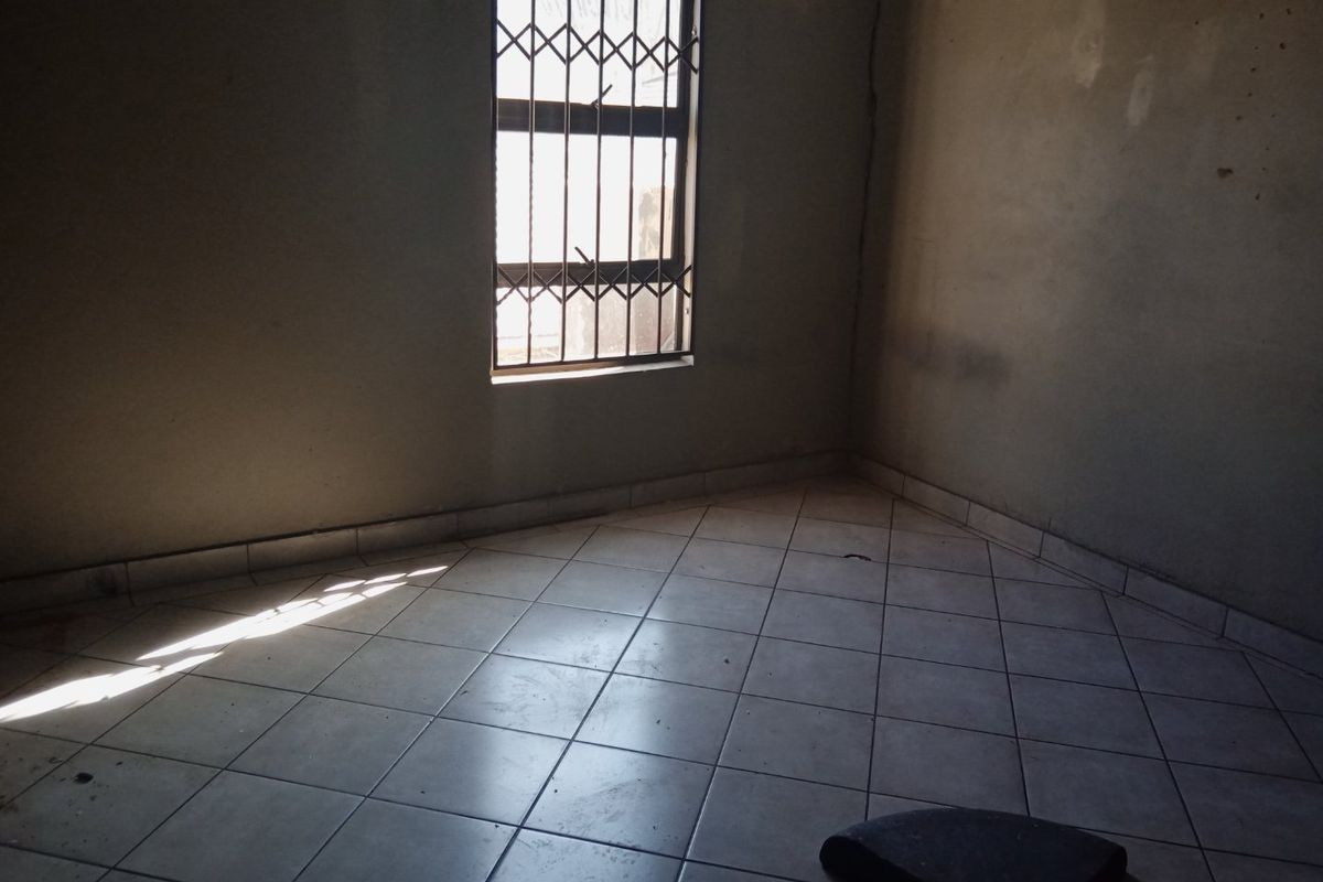 An empty bedroom featuring ceramic floor tiles and a window fitted with a security gate, requiring cosmetic updates to the wall finishes.