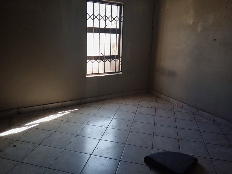 An empty bedroom featuring ceramic floor tiles and a window fitted with a security gate, requiring cosmetic updates to the wall finishes.