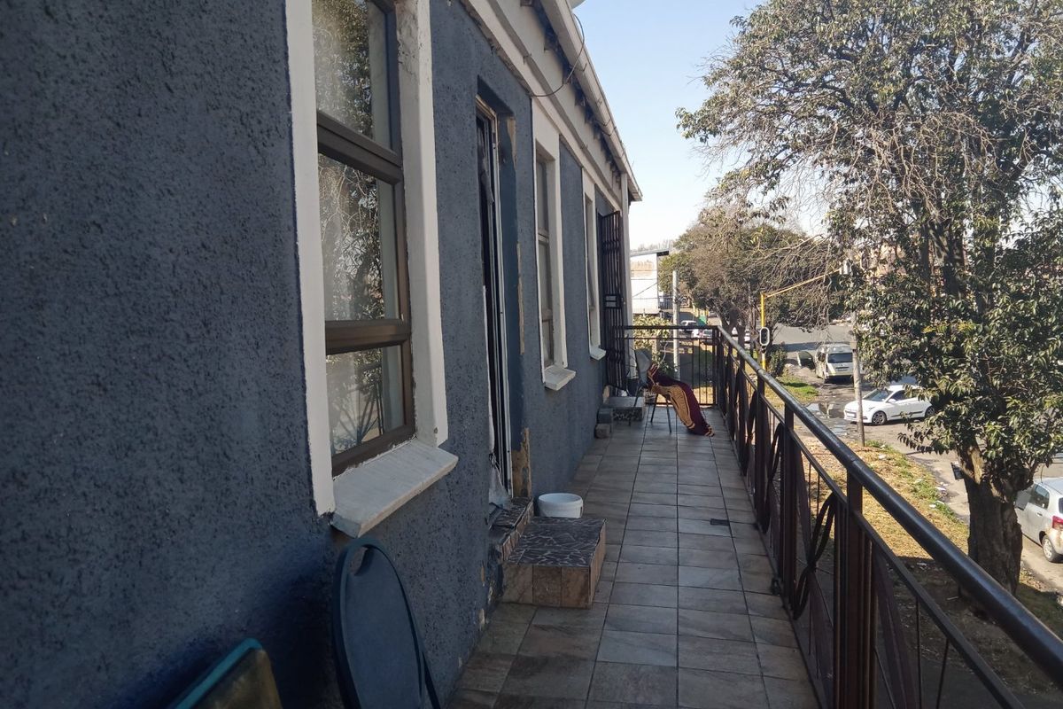 An exterior balcony featuring tiled flooring and a metal balustrade, overlooking the street with views of surrounding trees and urban infrastructure.