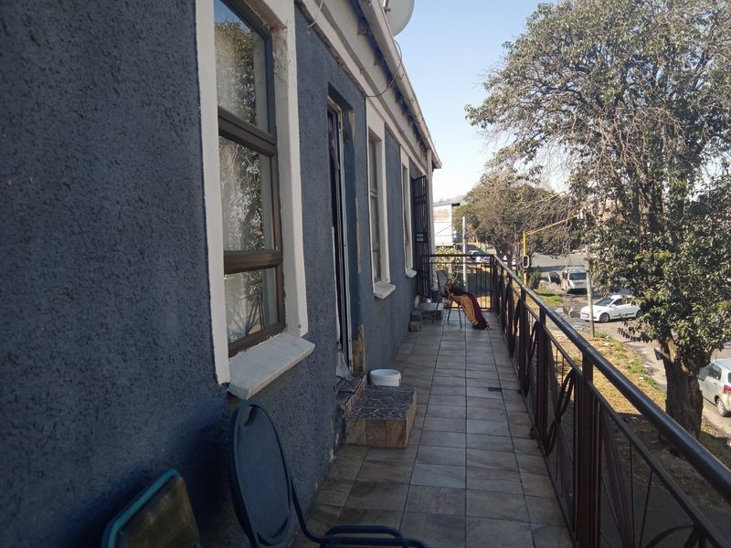 An exterior balcony featuring tiled flooring and a metal balustrade, overlooking the street with views of surrounding trees and urban infrastructure.