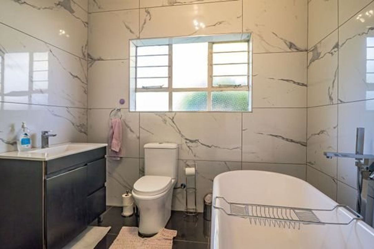 Modern bathroom featuring marble-look wall tiles, a sleek vanity cabinet, a freestanding bathtub, and contemporary chrome fixtures.