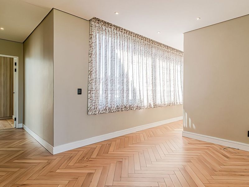 A bright, empty living area featuring high-quality herringbone timber flooring, neutral wall finishes, and recessed downlighting.