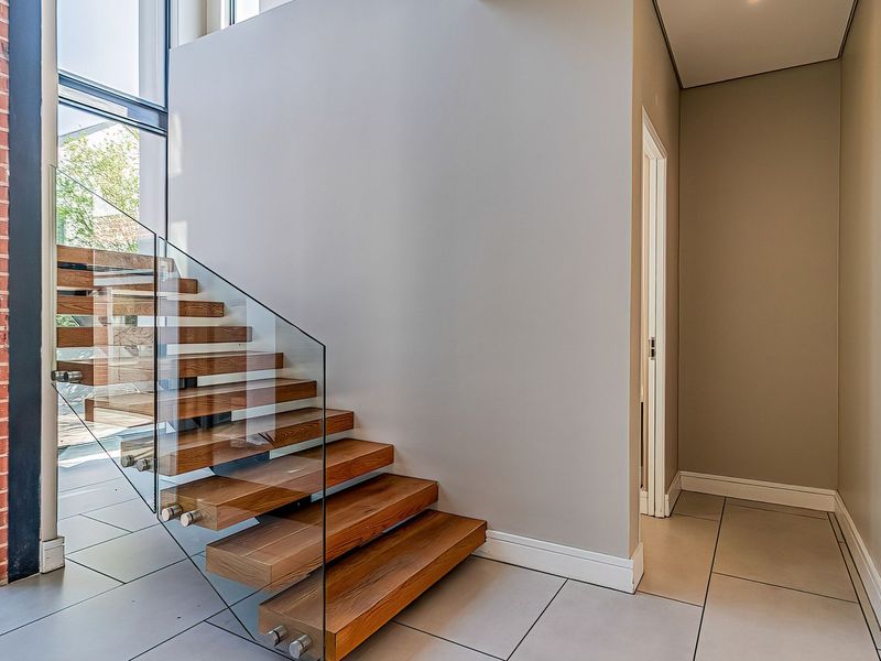 Modern entrance hall featuring a striking floating timber staircase with glass balustrade, large format floor tiles, and expansive floor-to-ceiling windows.