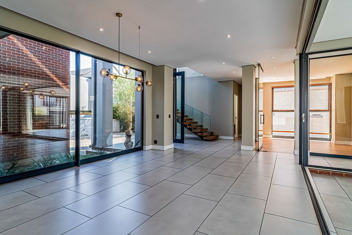 Spacious, modern open-plan living area featuring large format floor tiles, floor-to-ceiling glass doors, and a striking floating timber staircase with glass balustrade.