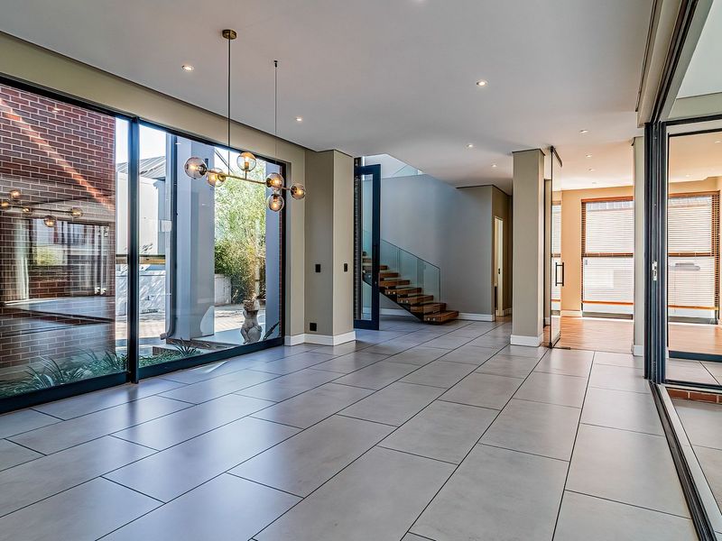 Spacious, modern open-plan living area featuring large format floor tiles, floor-to-ceiling glass doors, and a striking floating timber staircase with glass balustrade.