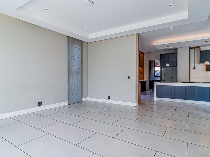 Spacious open-plan living area featuring large format floor tiles, a modern kitchen with island, and seamless access to outdoor space through sliding glass doors.