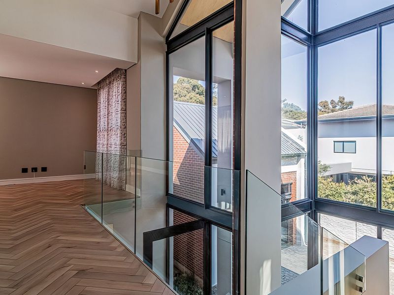 A bright, modern landing area featuring high-quality herringbone timber flooring, a sleek glass balustrade, and expansive floor-to-ceiling windows overlooking the exterior.