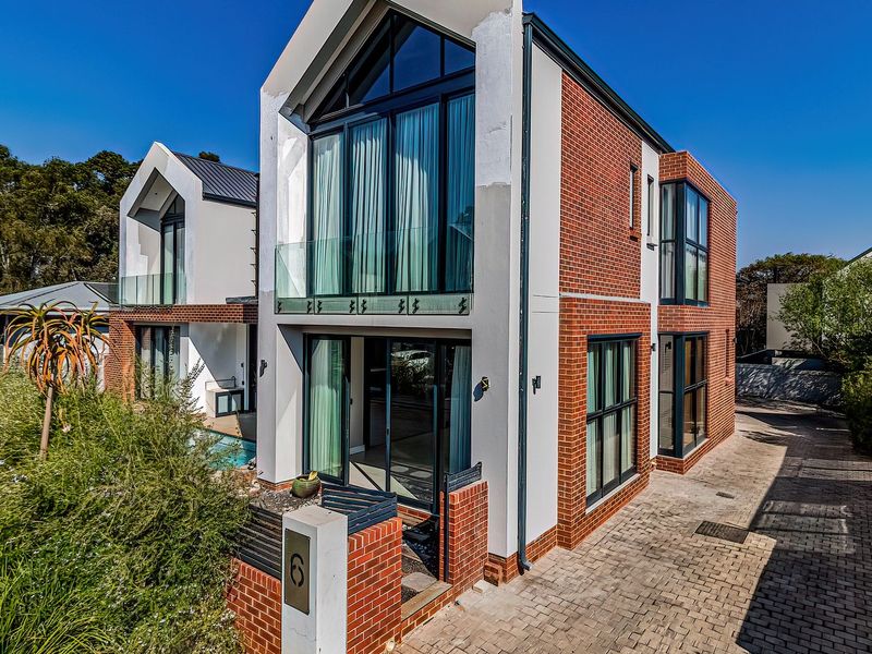 Modern multi-story residential property featuring a striking brick and render facade, large glass windows, and a paved driveway.