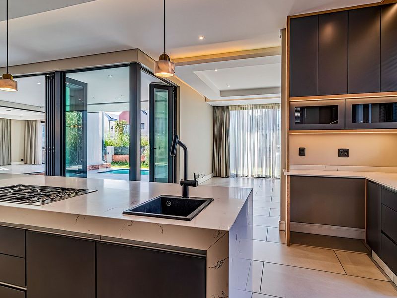 Modern open-plan kitchen featuring a large island with gas cooktop, sleek cabinetry, and seamless indoor-outdoor flow through bi-fold doors to the pool area.