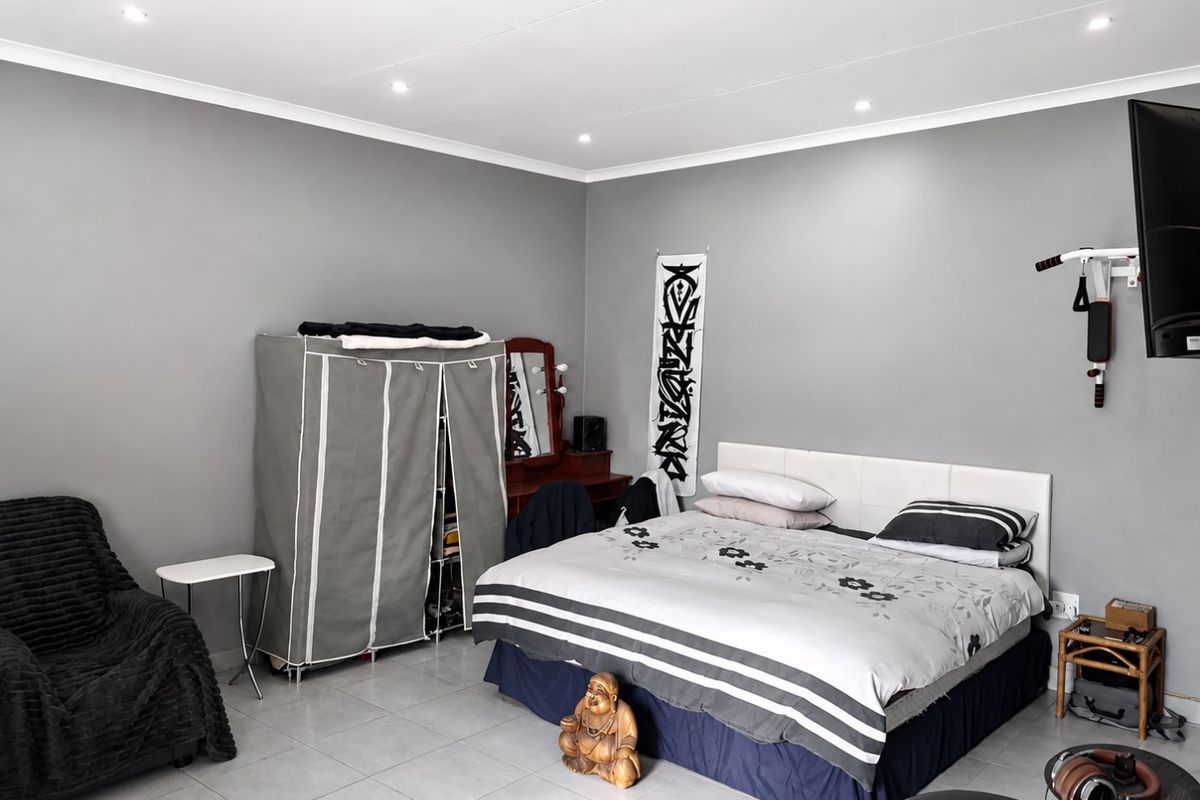 A spacious bedroom featuring neutral grey walls, tiled flooring, and recessed downlighting, offering a clean and functional living space.