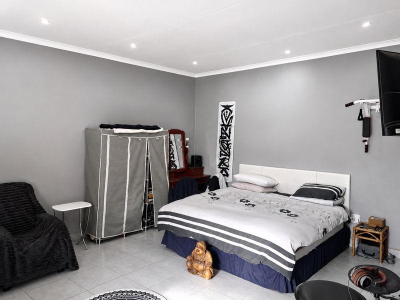 A spacious bedroom featuring neutral grey walls, tiled flooring, and recessed downlighting, offering a clean and functional living space.