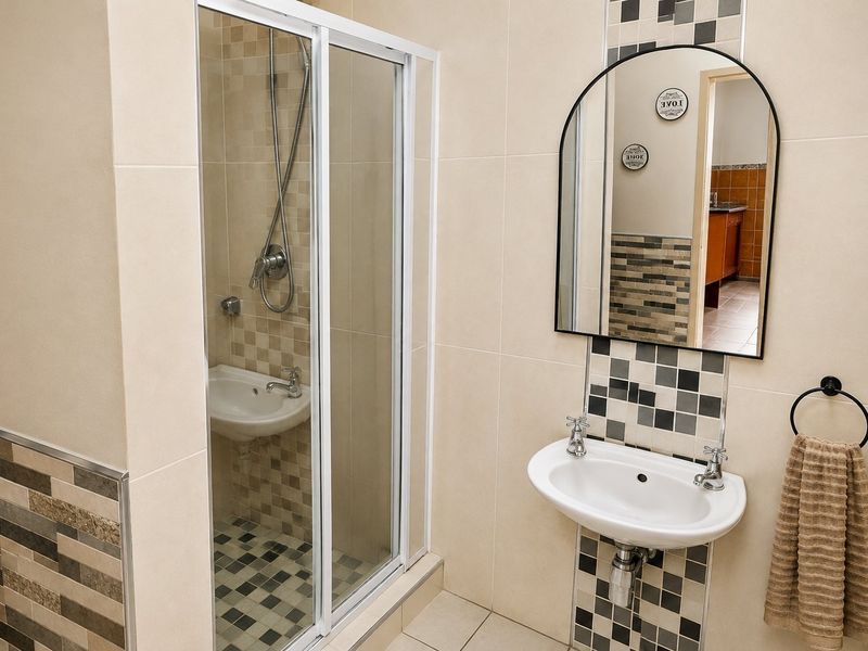 A clean, modern bathroom featuring a glass-enclosed shower, wall-mounted basin with chrome tapware, and decorative mosaic tile accents.