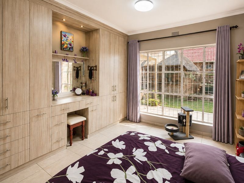 A well-maintained bedroom featuring extensive light wood built-in cabinetry with an integrated vanity station, tiled flooring, and large windows with security bars.