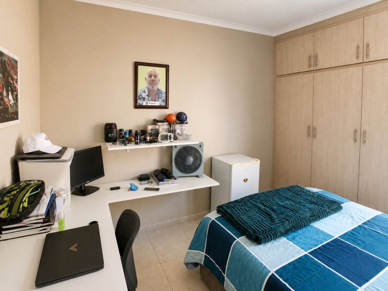 A functional bedroom featuring built-in wooden cupboards, tiled flooring, and a built-in desk area, providing practical storage and workspace solutions.