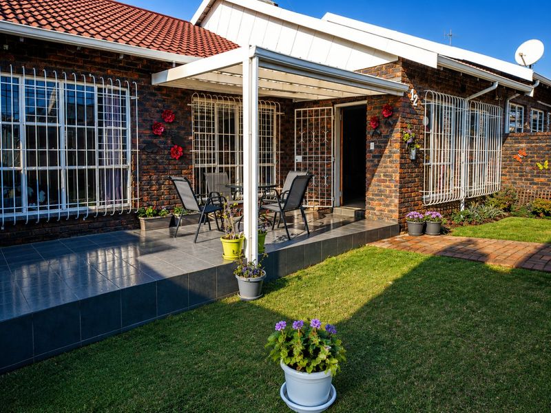 A well-maintained rear exterior view of the townhouse featuring a tiled patio, covered outdoor area, and a neat garden lawn.