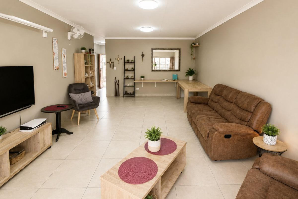 A spacious, well-maintained living room featuring neutral tiled flooring, recessed ceiling lighting, and a functional built-in wall desk area.