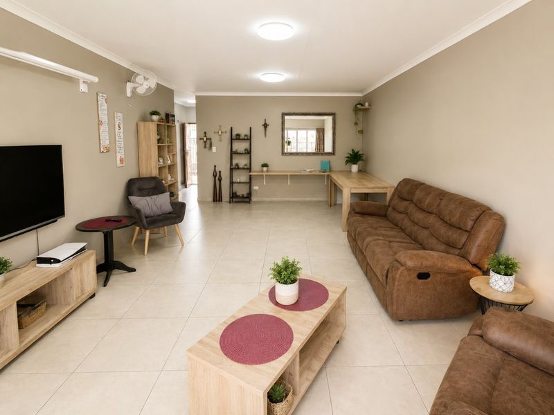 A spacious, well-maintained living room featuring neutral tiled flooring, recessed ceiling lighting, and a functional built-in wall desk area.
