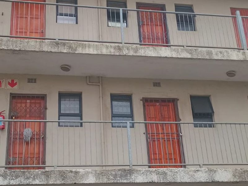 Exterior view of a multi-story apartment building featuring concrete walkways, metal security gates, and ground-level roller garage doors.