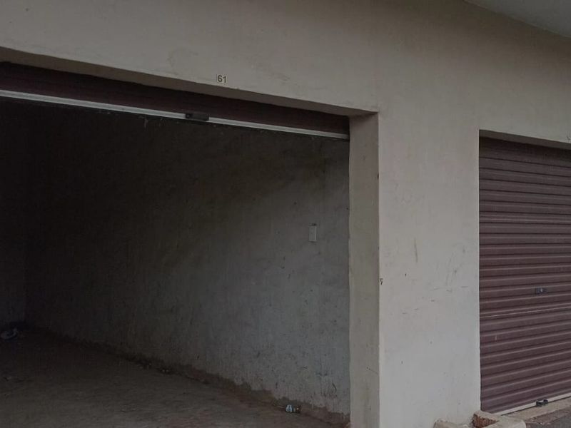 A row of garage units featuring roller shutter doors and concrete flooring, showing signs of exterior wear and surface staining.