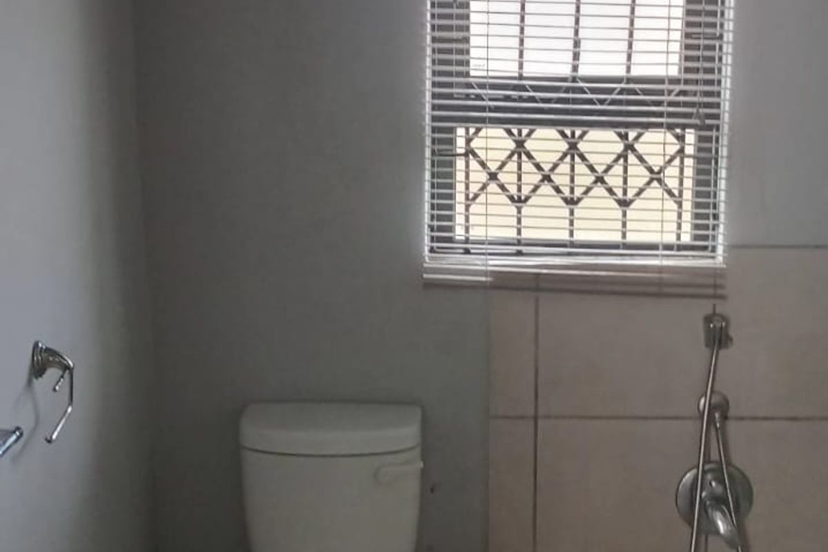A functional bathroom featuring a standard toilet, bathtub with handheld shower mixer, and tiled splashback, requiring cosmetic updates to improve its overall condition.